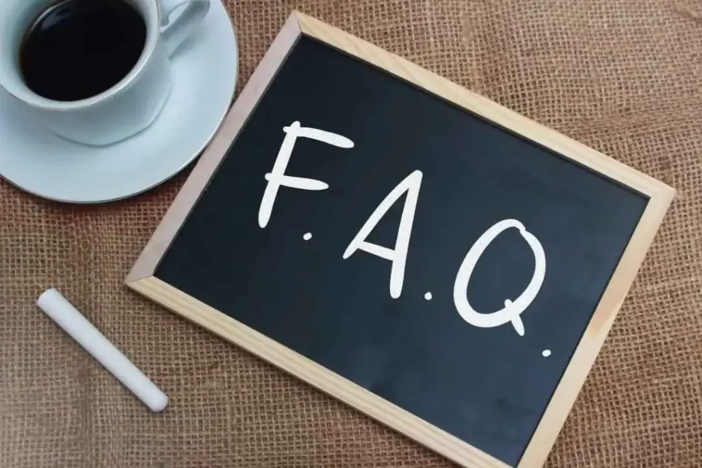 A chalkboard with "F.A.Q." written on it, next to a cup of coffee and a piece of chalk on a burlap surface.