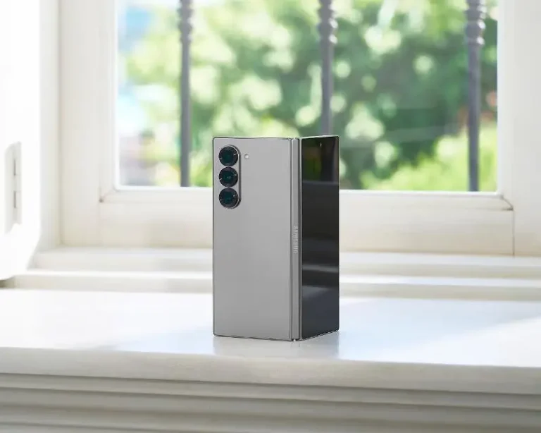 A Samsung Galaxy Z Fold 6 smartphone is standing partially open on a windowsill with a blurred outdoor background.