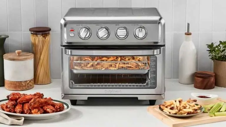 A Cuisinart TOA-70 oven with fries cooking inside, surrounded by plates of chicken wings and fries, and jars of pasta and other ingredients on the kitchen counter.